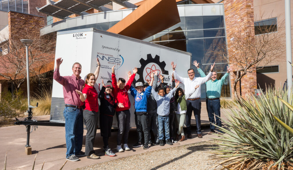 student and teachers with arms raised in front of Tech Trekker trailer